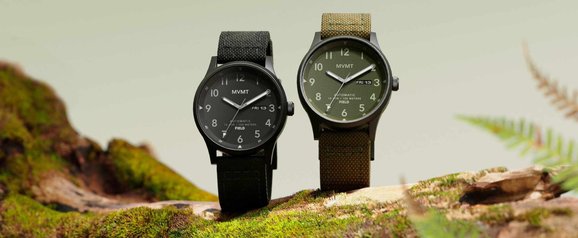 Two MVMT Field automatic watches in black and green standing straight up on a mossy rock in the wild