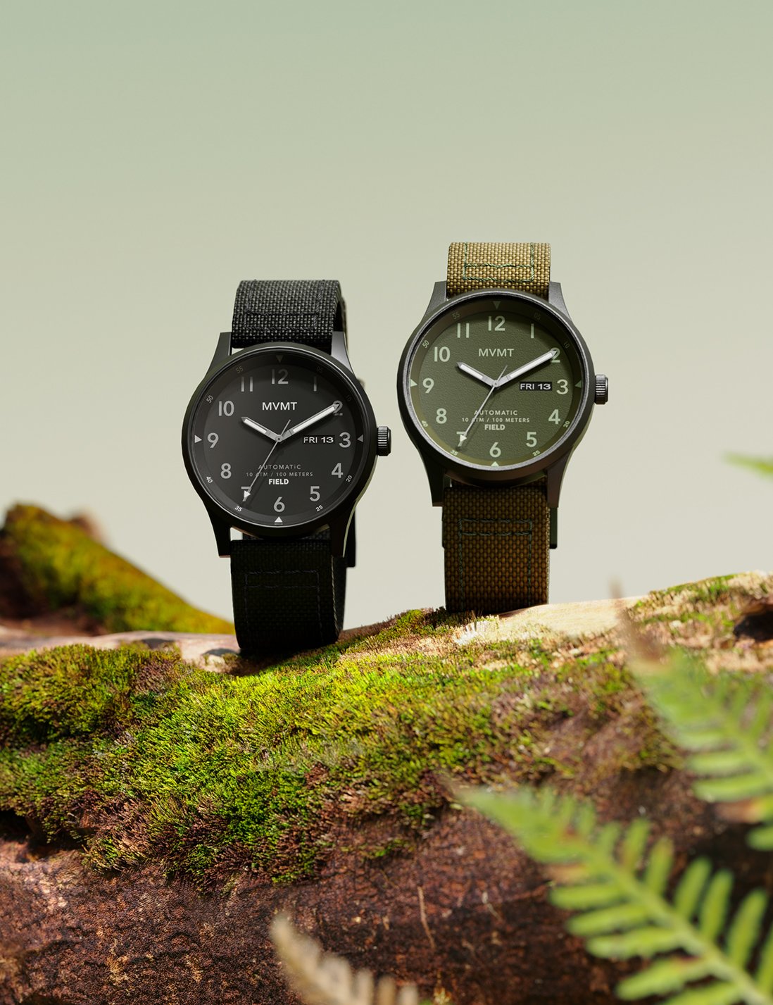 Two MVMT Field automatic watches in black and green standing straight up on a mossy rock in the wild