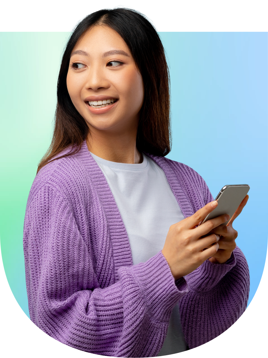 A woman smiles while holding her phone, looking off into the distance.