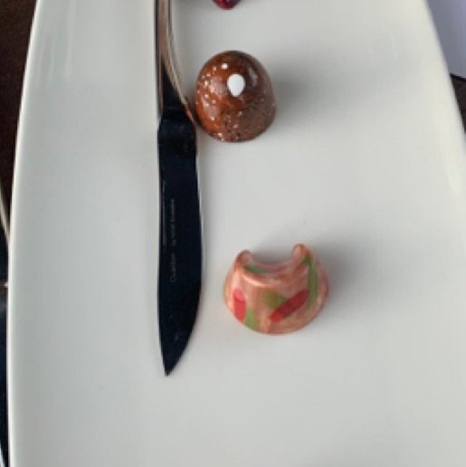  Two, beautifully shiny, hand painted chocolate truffles sit on a white plate, a silver knife lying next to them.