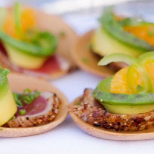 Small crackers with thin slices of seared tuna, garnished with avocado and orange slices.