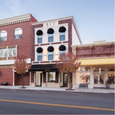  A narrow, three story, brick building with black domed awnings, the JUSTIN logo in gold on the largest window.