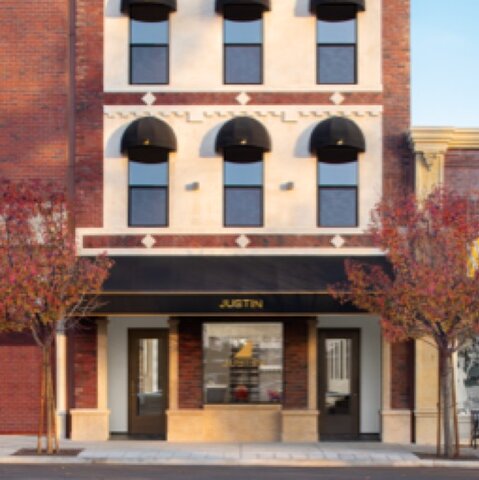 A narrow, three story, brick building with black domed awnings, the JUSTIN logo in gold on the largest window.