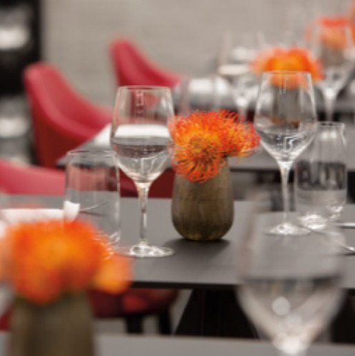 Black tables with red chairs, orange spiked flowers in copper vases, and empty wine glasses.