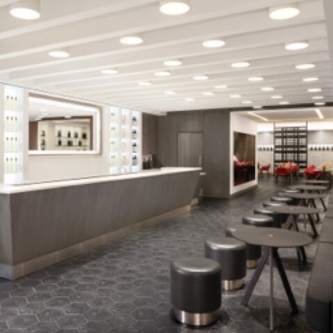 A white ceiling looms over a gray and white wine bar across from a black bench, small round tables, and black stools. 