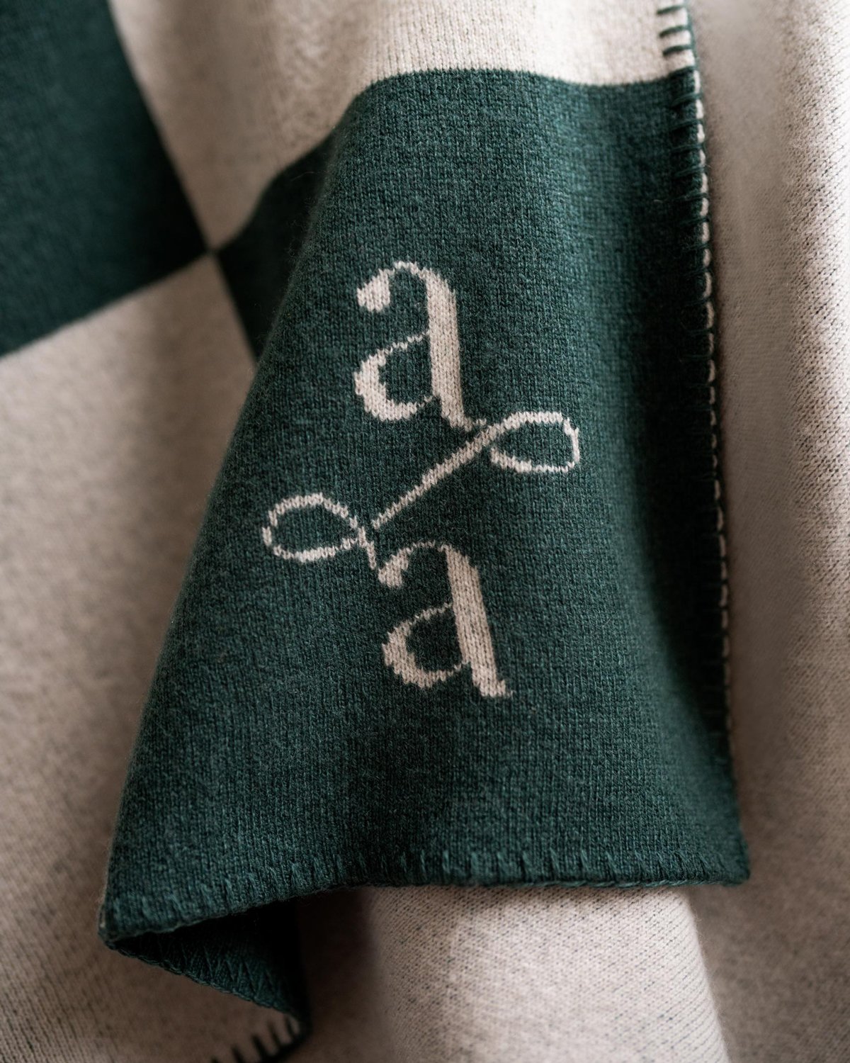 Designed and monogrammed Atria touchpoint. A green and white checkered blanket with visible seams and a script logo
