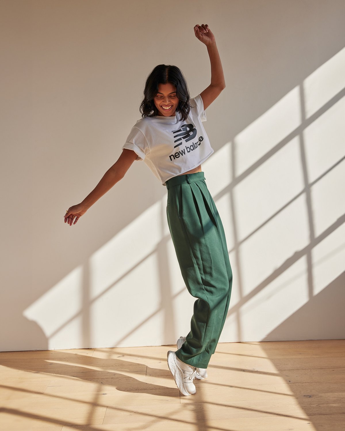 Model dancing in a New Balance t-shirt, green dress pants, and new white kicks