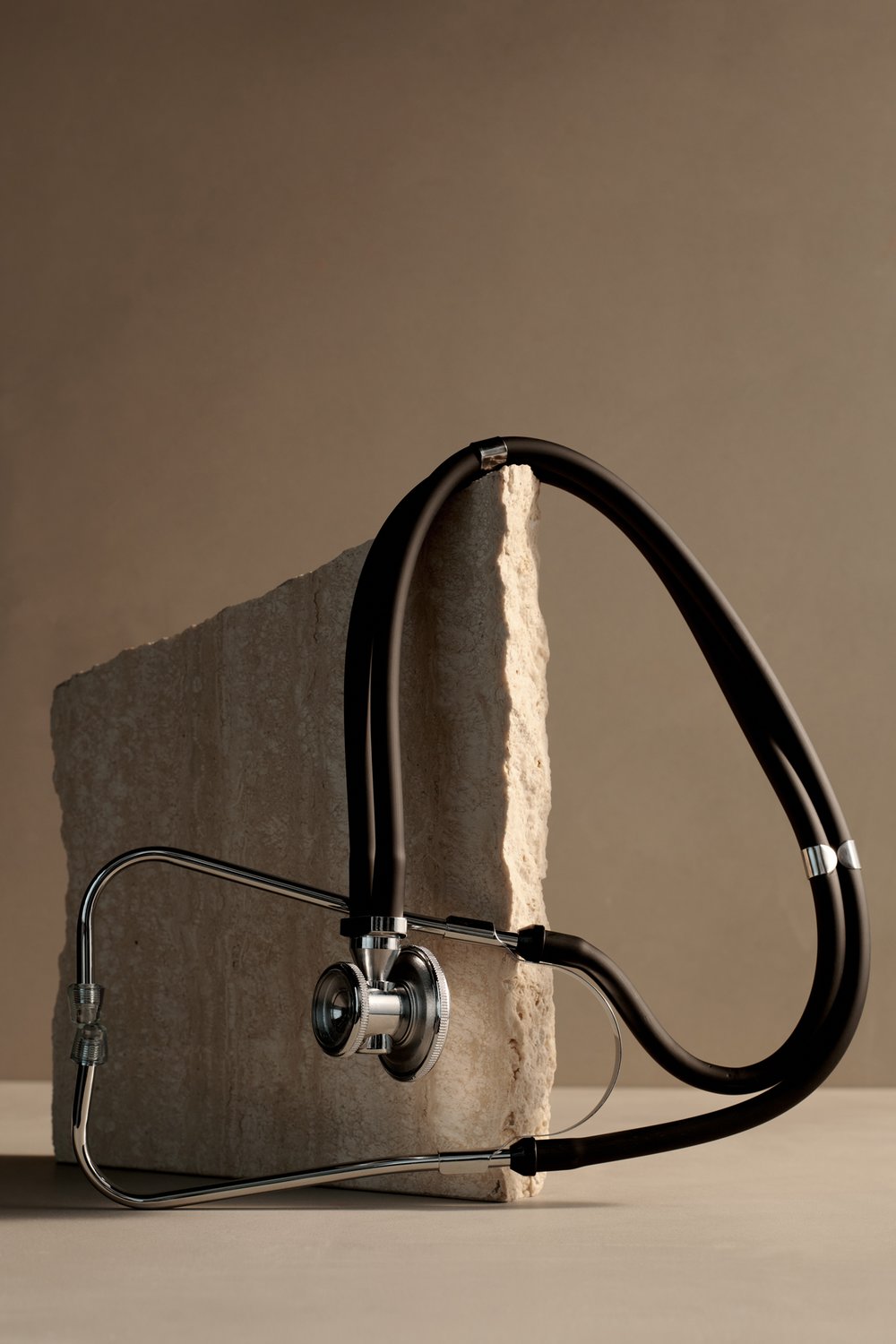 Metallic and black stethoscope on a rock with a neutral background to convey balance and nature in Atria’s healthcare space.