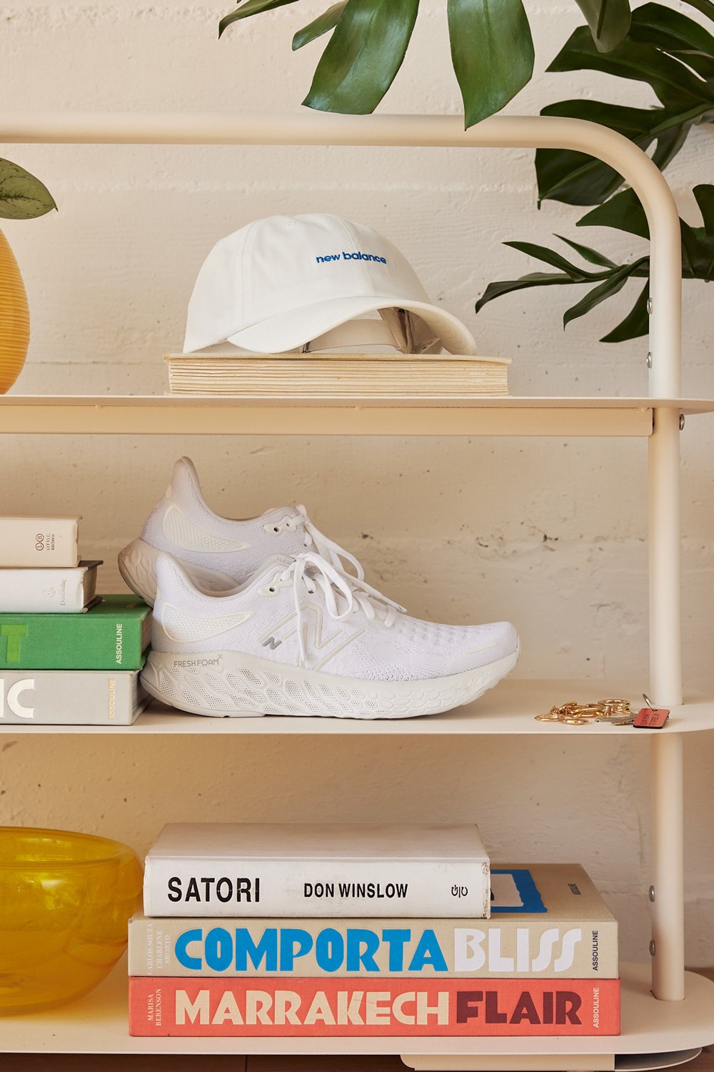 White tennis shoes and baseball cap with New Balance logos on a bookshelf 