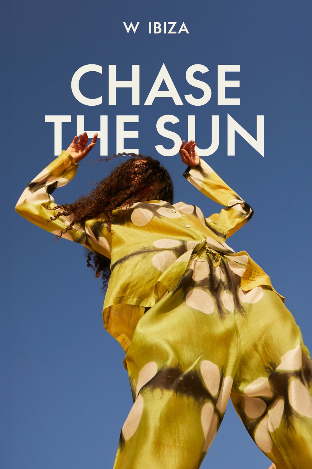 A woman in a yellow matching set dancing under a blue sky in Ibiza. Text reads W Hotels Ibiza: Chase the Sun to promote travel to this Spain location