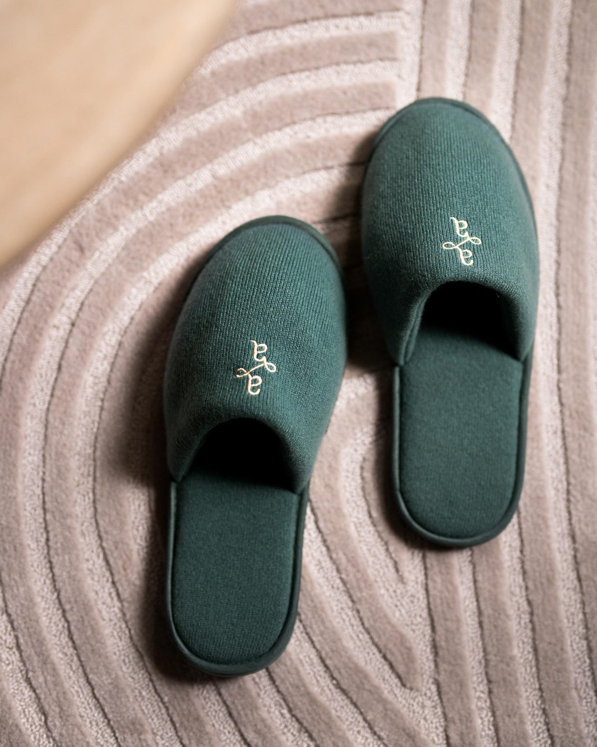 Branded merchandise carefully made for Atria, including comfortable monogrammed green teal slippers on a cozy and soft grey carpeted floor