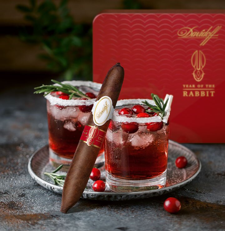 2 glasses of Cranberry Old Fashioned. A Davidoff Year of the Rabbit Limited Edition perfecto cigar leans against one of them.