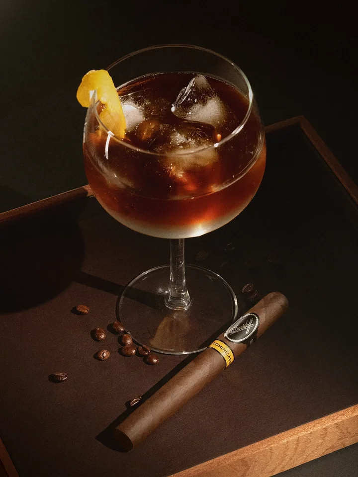 Mocktail cigar pairing with a Cold Fashioned: vanilla-cappuccino samba. Cold brew, syrup, orange bitters over ice match the cigar beside coffee beans and glass.
