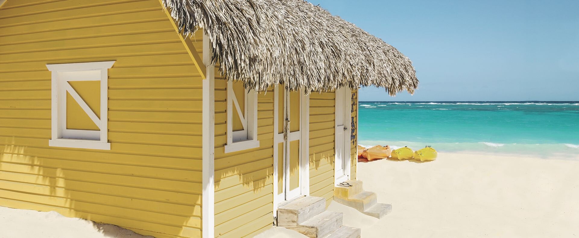 View of a beach house on the beach with a thatched roof and a turquoise sea. 