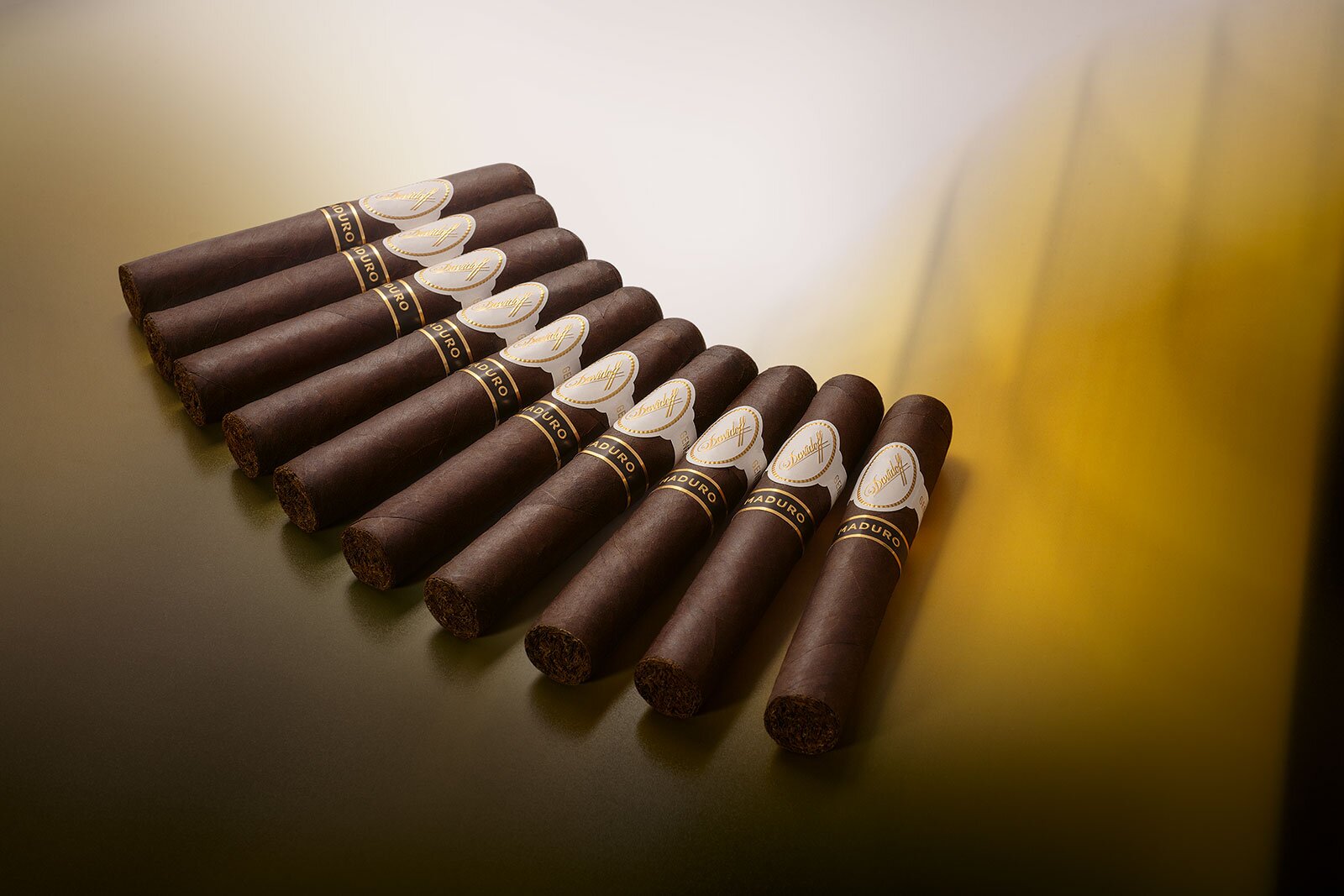 A row of neatly arranged dark brown cigars, showcasing elegant labels and an ambient golden background.