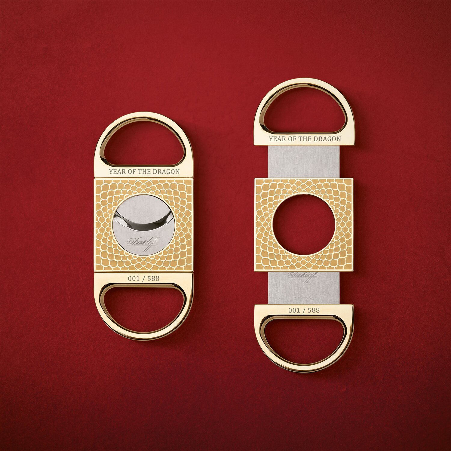 Two cigar cutters next to each other on a red background. A closed and an open Davidoff Year of the Dragon double-blade cutter next to an open one.