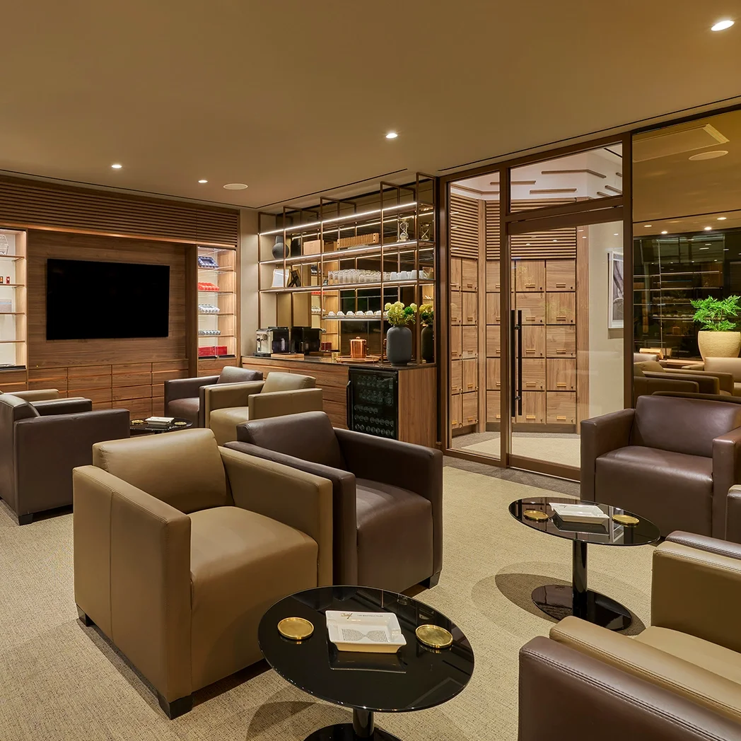 An elegant cigar shop with wooden shelves stocked full of cigar boxes, a circular table displaying premium cigars, and tobacco leaves hanging above.