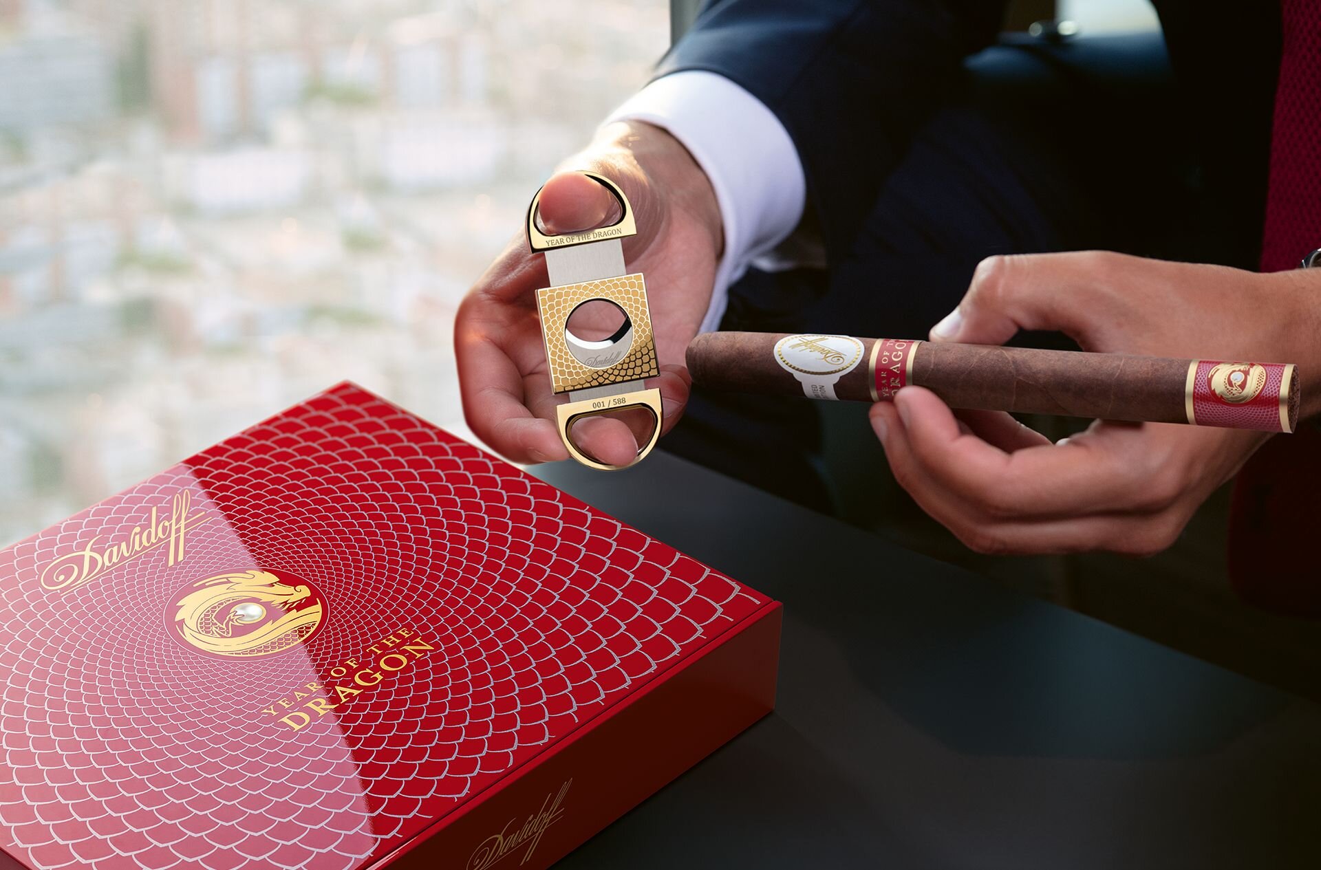 An open Davidoff Year of the Dragon double-blade cutter, next to it a man trying to cut off the tip of the cigar. It is a close-up of the cutter and the cigar. 