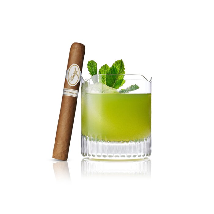 An Agave Green Cocktail served in a Winston Churchill glass, with an Aniversario No. 3 cigar elegantly leaning against the glass, highlighting a refined pairing of drink and luxury cigar.