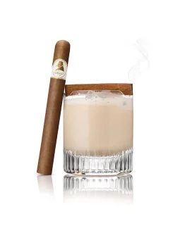 Cream of Rum cocktail with frothy top beside a gold-labeled cigar, exuding elegance.