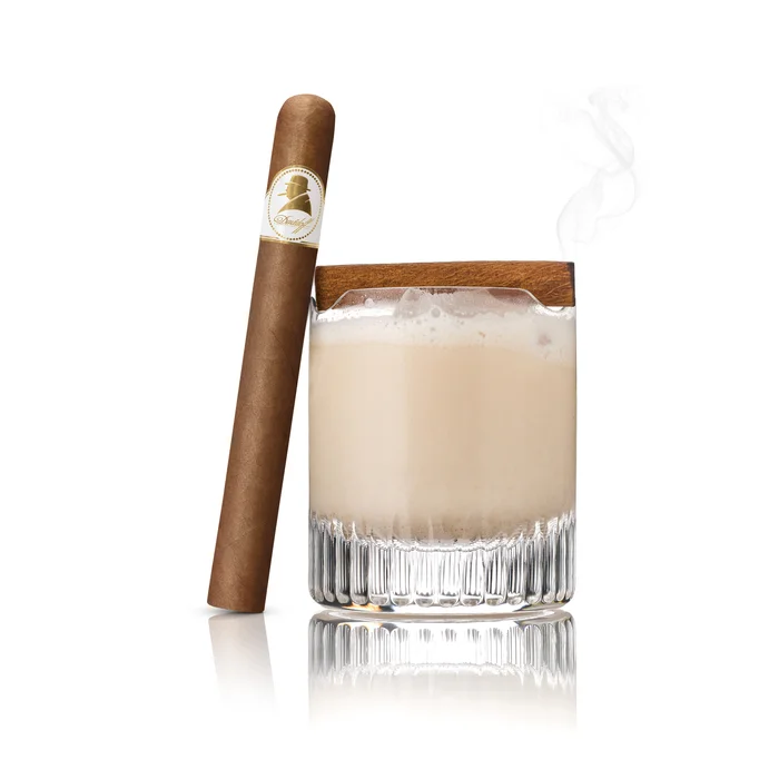 Cream of Rum cocktail with frothy top beside a gold-labeled cigar, exuding elegance.