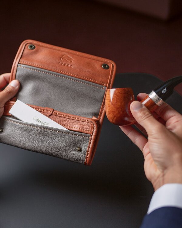 A close-up captures the exquisite pipe tobacco pouch crafted from nappa and bovine suede, with a hand holding a pipe nearby.