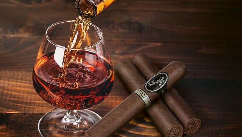 3 Davidoff Limited Edition 2022 cigars and a glass filled with rum on a wooden surface.
