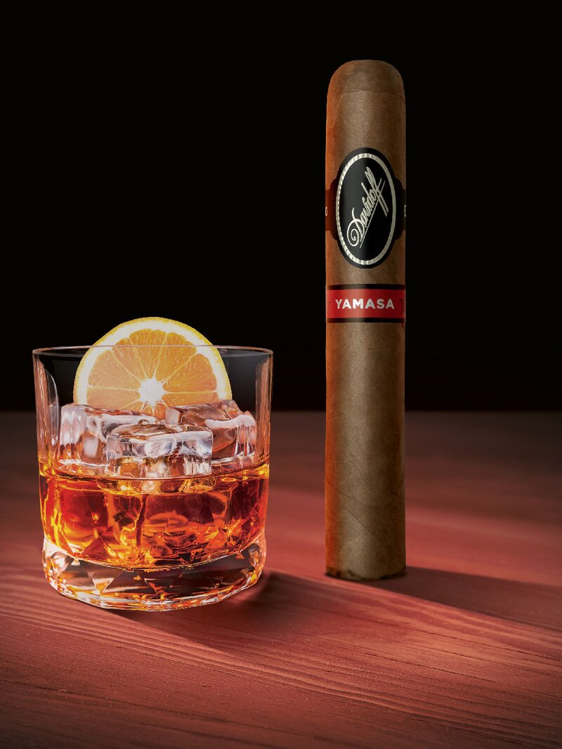 A Davidoff Yamasá cigar standing upright next to a glass with whisky.