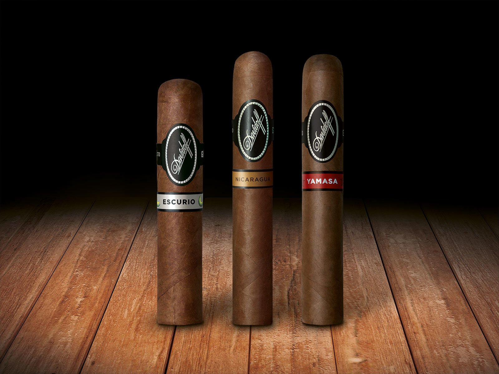 Three Black Band Collection cigars (Escurio, Nicaragua & Yamasa) standing on a wooden floor.