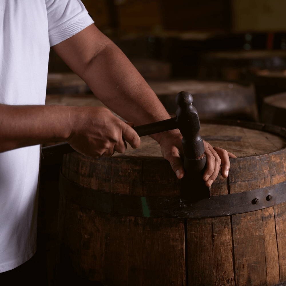 A rum cask that is being closed by a person using a special tool.