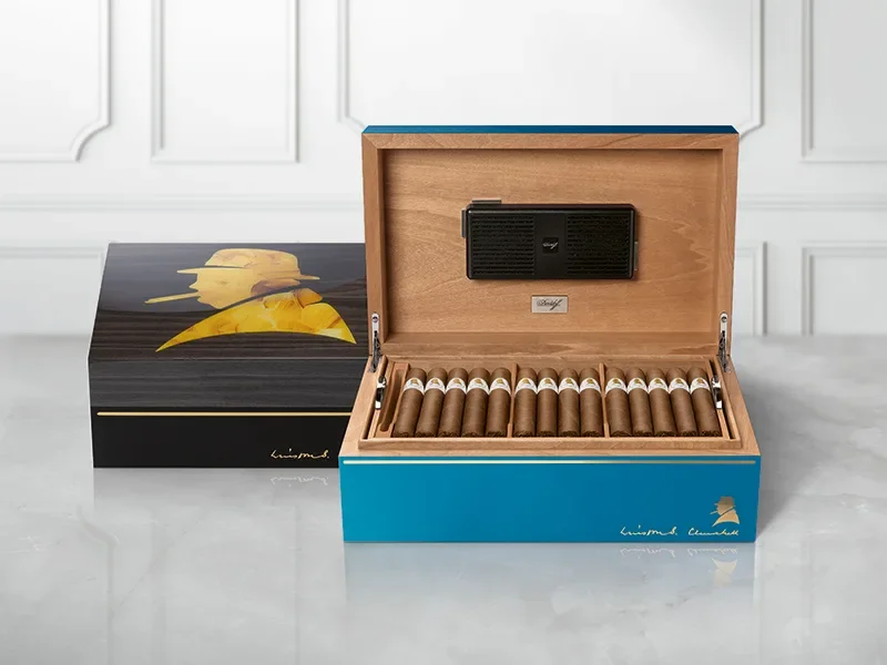 Der dunkelgraue Davidoff Winston Churchill Humidor im Primos-Format steht hinter dem blauen Ambassador-Format. Der Ambassador ist geöffnet und zeigt Zigarren.