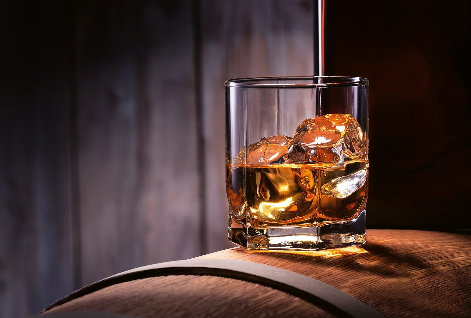 A glass of amber whiskey with ice cubes, captured in warm lighting against a dark wooden background.