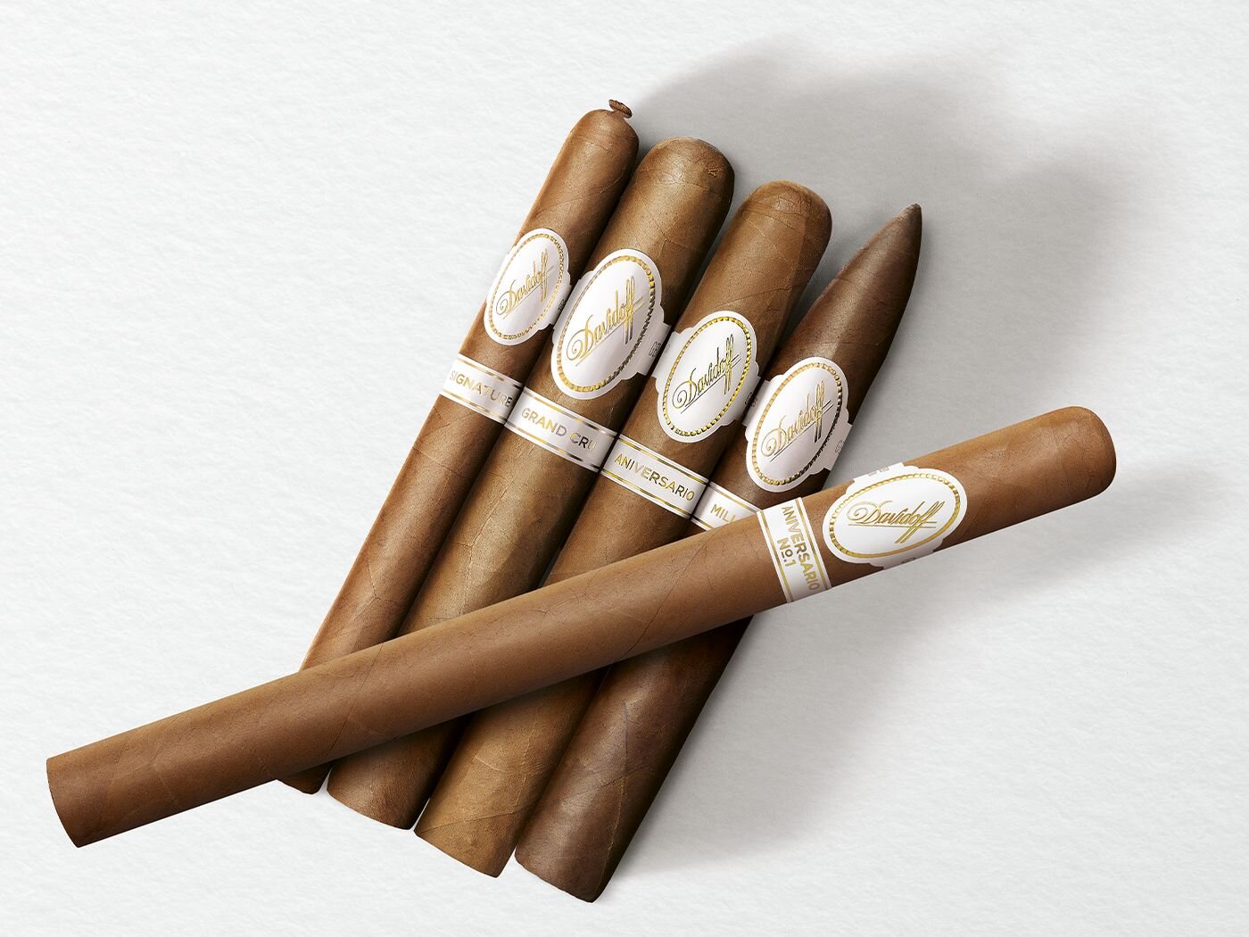 4 cigars of the Davidoff White Band Collection lines Signature, Grand Cru, Millennium and Aniversario with one Davidoff Aniversario No. 1 Limited Edition Collection cigar placed across on top of them. 