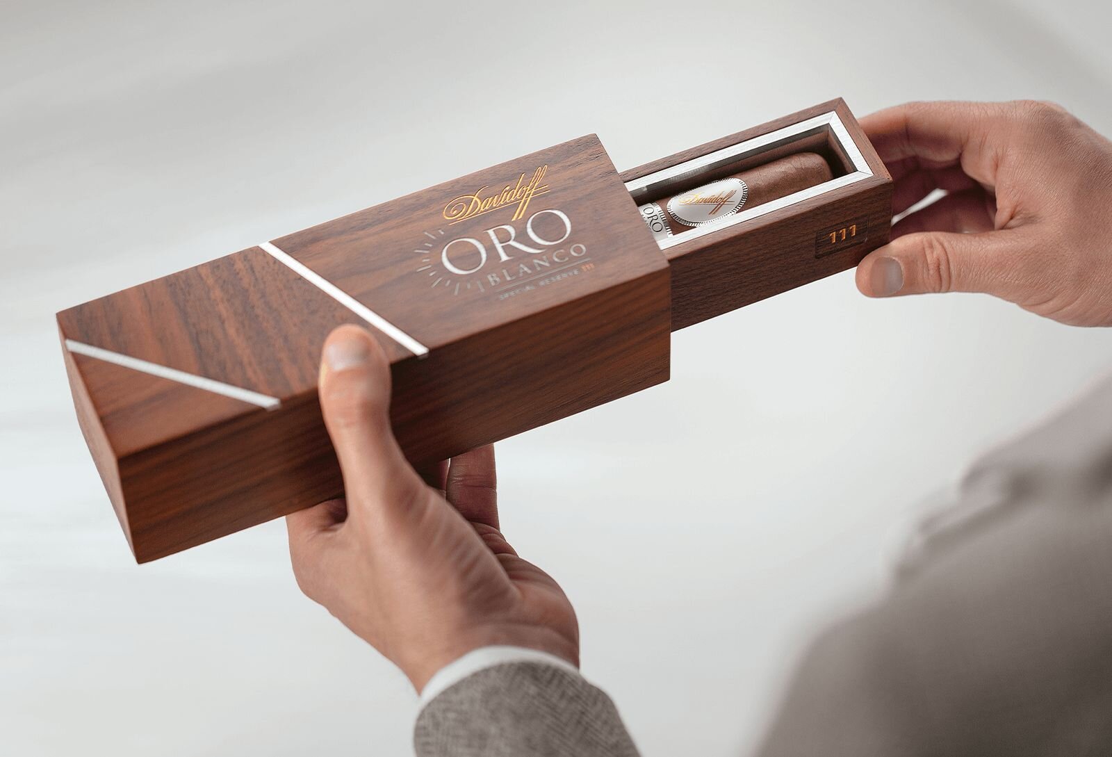 An overhead view of the open packaging for the ‘Oro Blanco Special Reserve 111 Years’ cigar, revealing a single cigar nestled inside. The packaging is held in the hand of a businessman, showcasing the cigar's elegance and premium presentation.