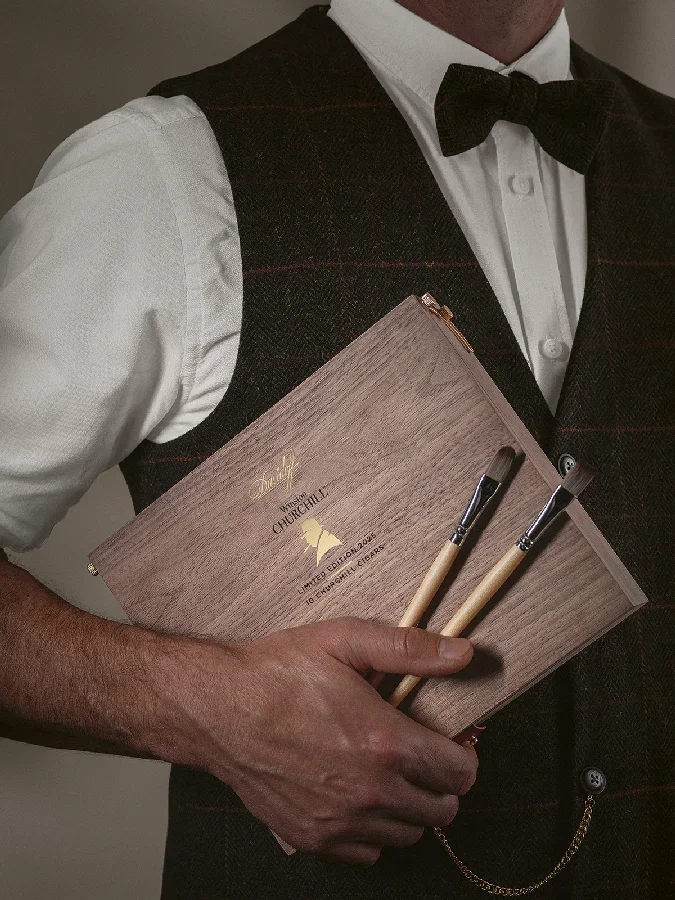 A man holding the box of the Winston Churchill Limited Edition alongside two paintbrushes.