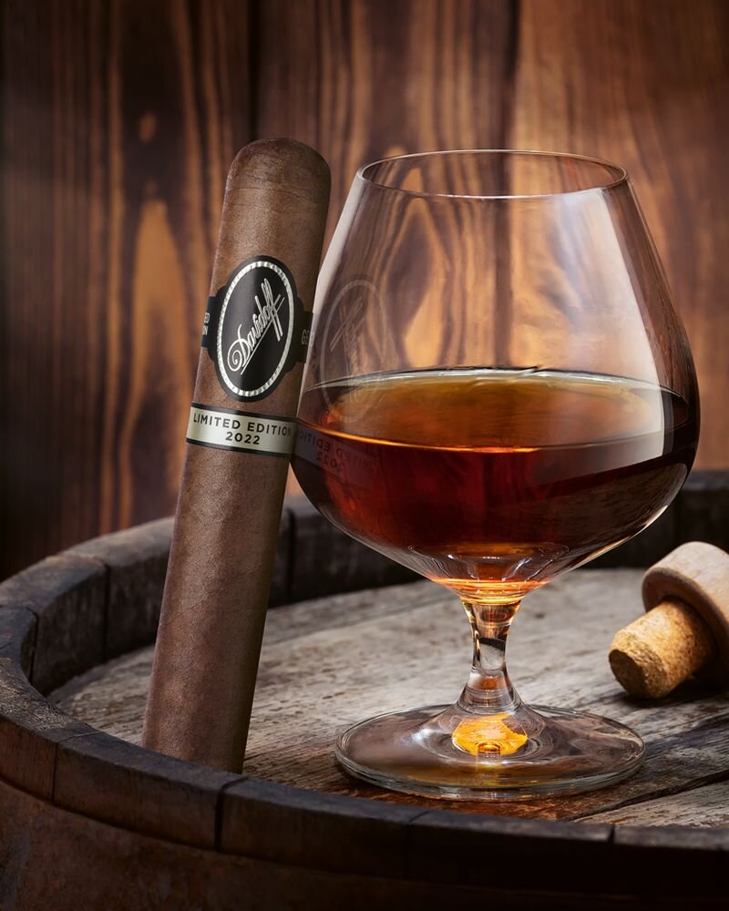 Glass filled with rum placed on a barrel with the Davidoff Limited Edition 2022 Gran Toro cigar standing next to it.
