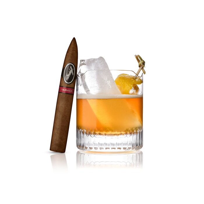 An Smoked High Tea Cocktail served in a Winston Churchill glass, with an Davidoff Yamasa Piramide cigar elegantly leaning against the glass, highlighting a refined pairing of drink and luxury cigar.