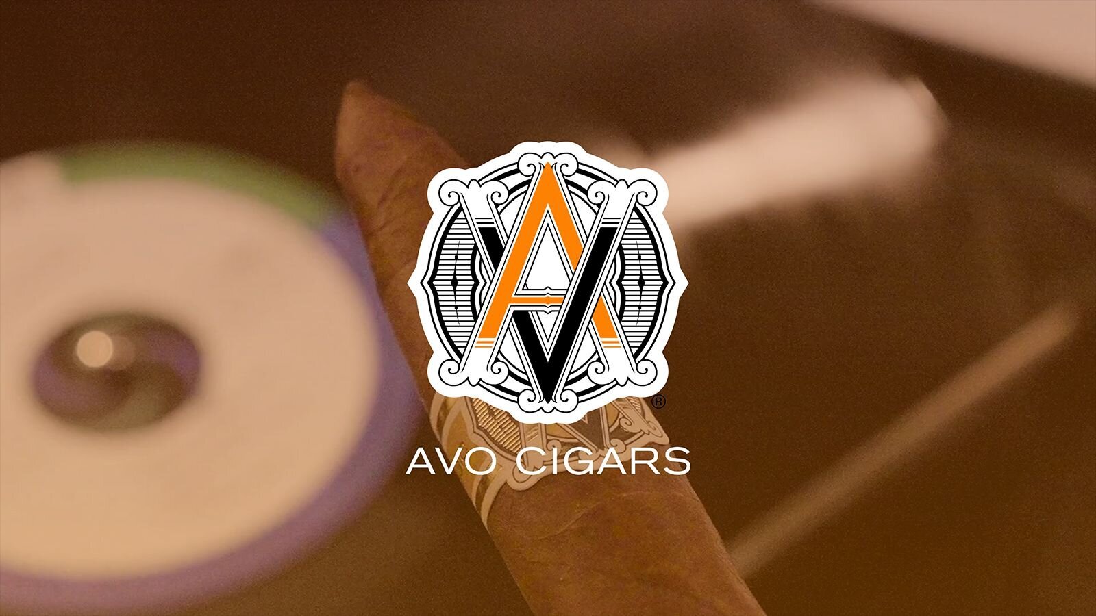 A close-up of an AVO Cigars cigar with the brand logo prominently displayed, set against a soft, blurred background.