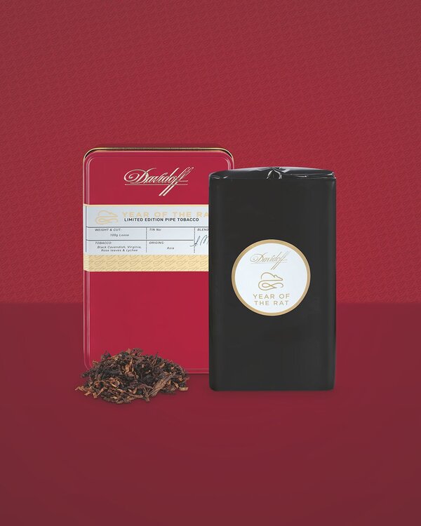 A front view of pipe tobacco in a bright red lacquered tin and a blend influenced by Asian flavors. In front of the tin is a stack of pipe tobacco.
