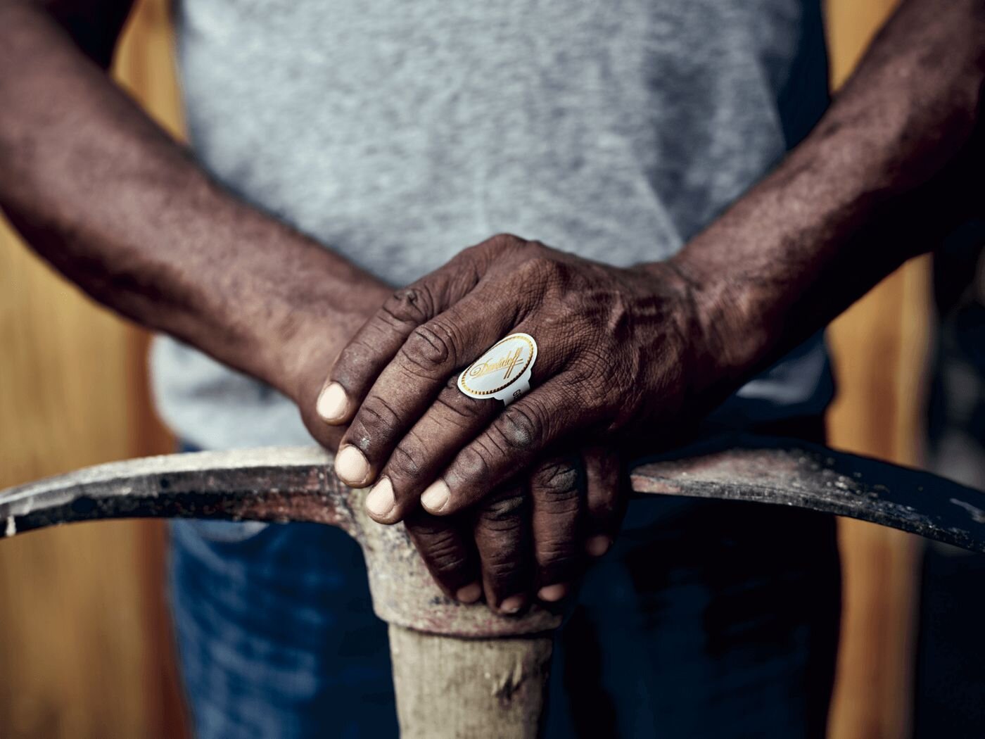 Davidoff Difference Image of a farmer leaning his hands on a pickaxe with a Davidoff white band ring on the ring finger.