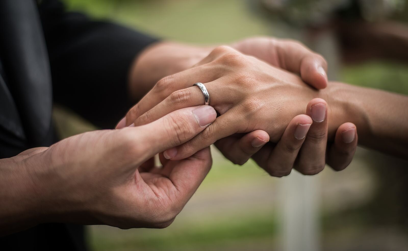  Close-up of hands as a valuable engagement ring is gently placed on the finger.
