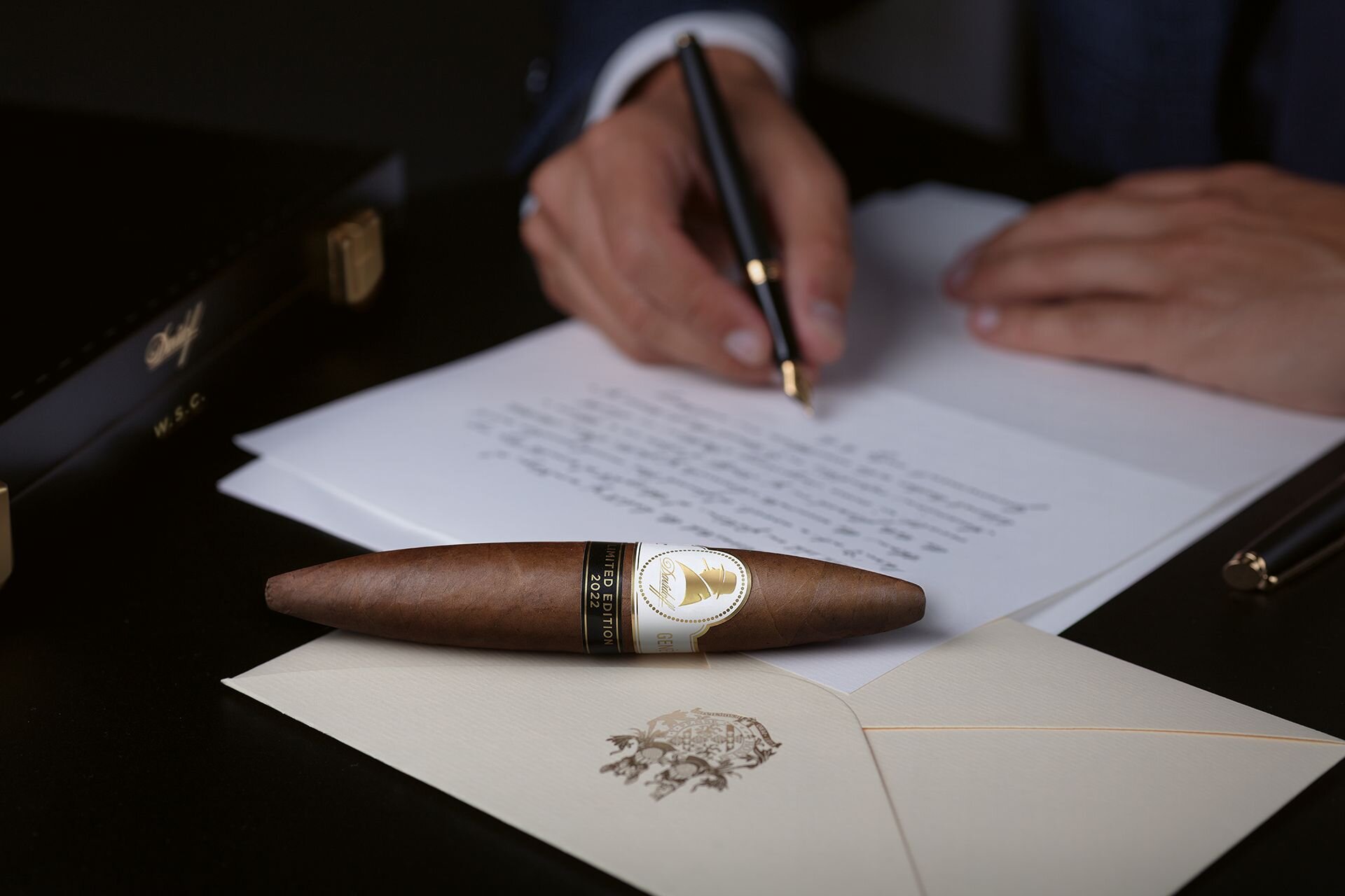 Davidoff Winston Churchill Limited Edition 2022 perfecto cigar on top of an envelope and a hand writing a letter in the background.