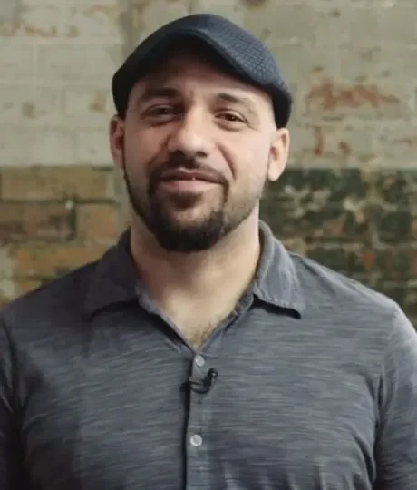 A smiling man with a beard and a hat, exuding a friendly and cheerful demeanor.