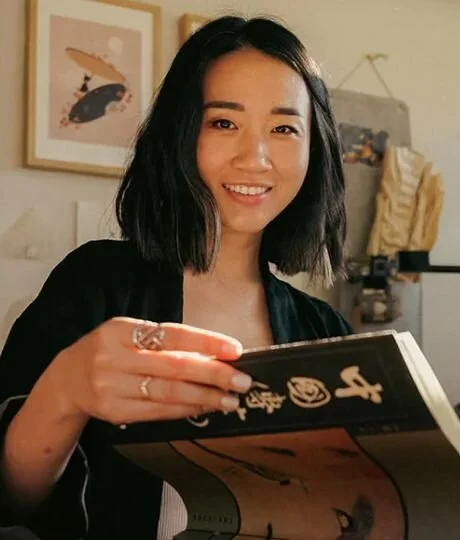  A woman smiles while holding a book in her hand, exuding joy and enthusiasm for reading.