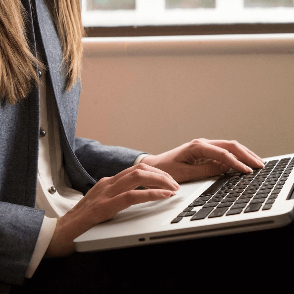 A close-up photo of a female  clinician using a laptop to look up how to write therapy progress notes.