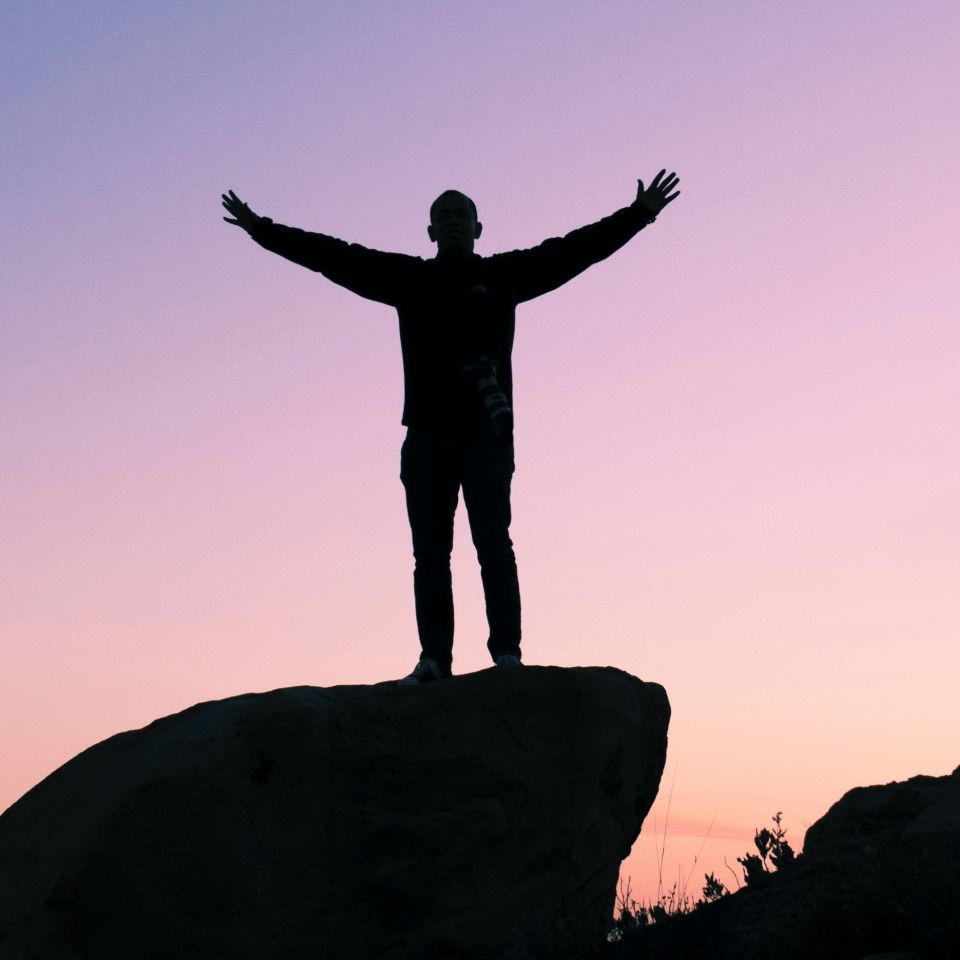 Person standing on top of a rock at sunset to build their self esteem