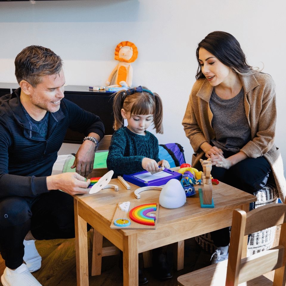 A mother and father sit at table with their daughter, who is seeing a speech-language pathologist that uses SOAP notes for speech therapy