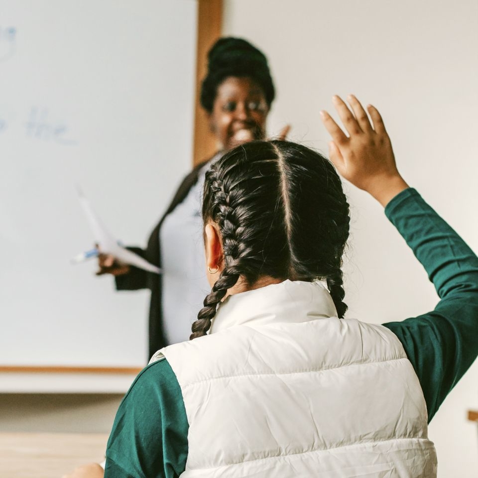 Female student raising her hand to talk with the teacher about her excuse absence letter