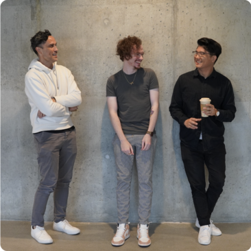 three simplepractice team members standing next to a concrete wall laughing