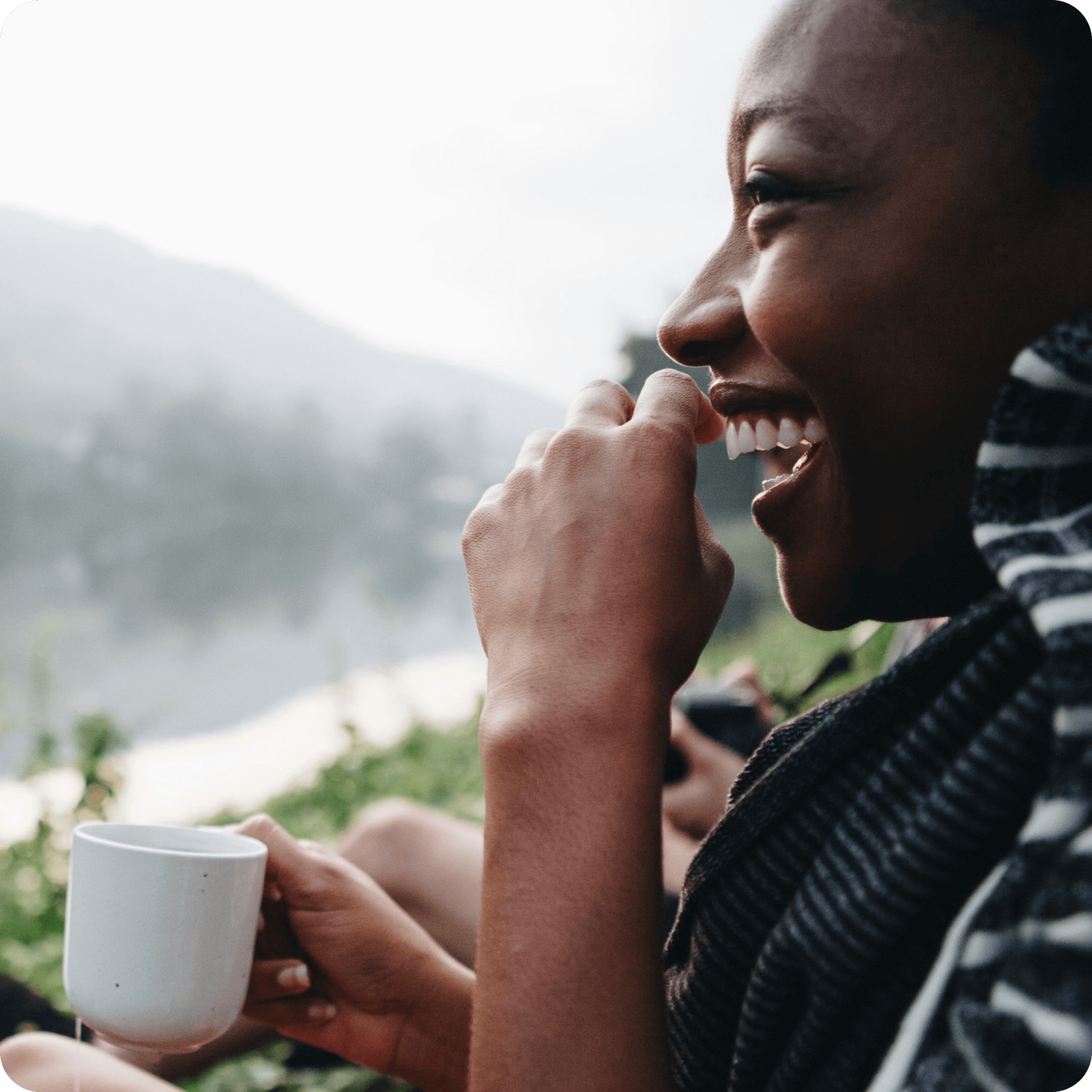 woman smiling while drinking from a mug and looking at a nice view
